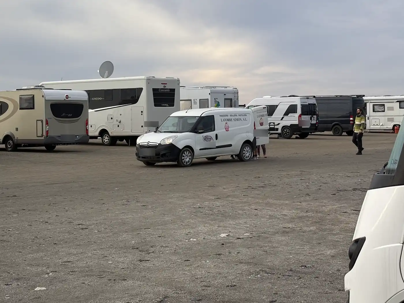 Weißer Lieferwagen einer spanischen Bäckerei auf einem Strandparkplatz in der Provinz Almería, dahinter mehrere Wohnmobile