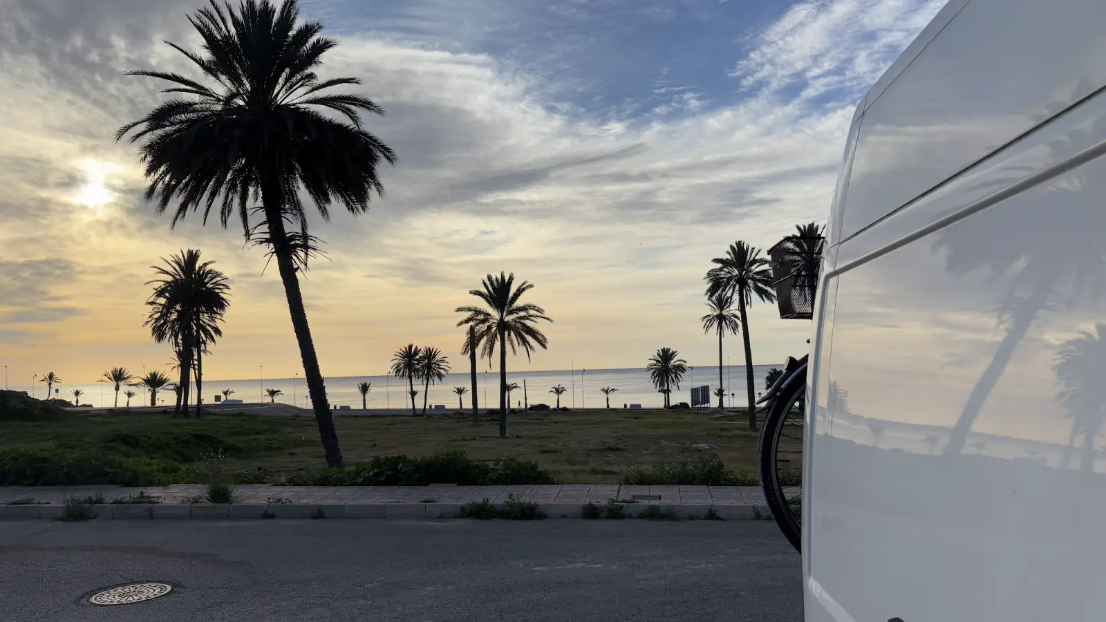 Unser Kastenwagen am Abend an einer Promenade an der Costa Cálida, davor Palmen und das Meer im Sonnenuntergang