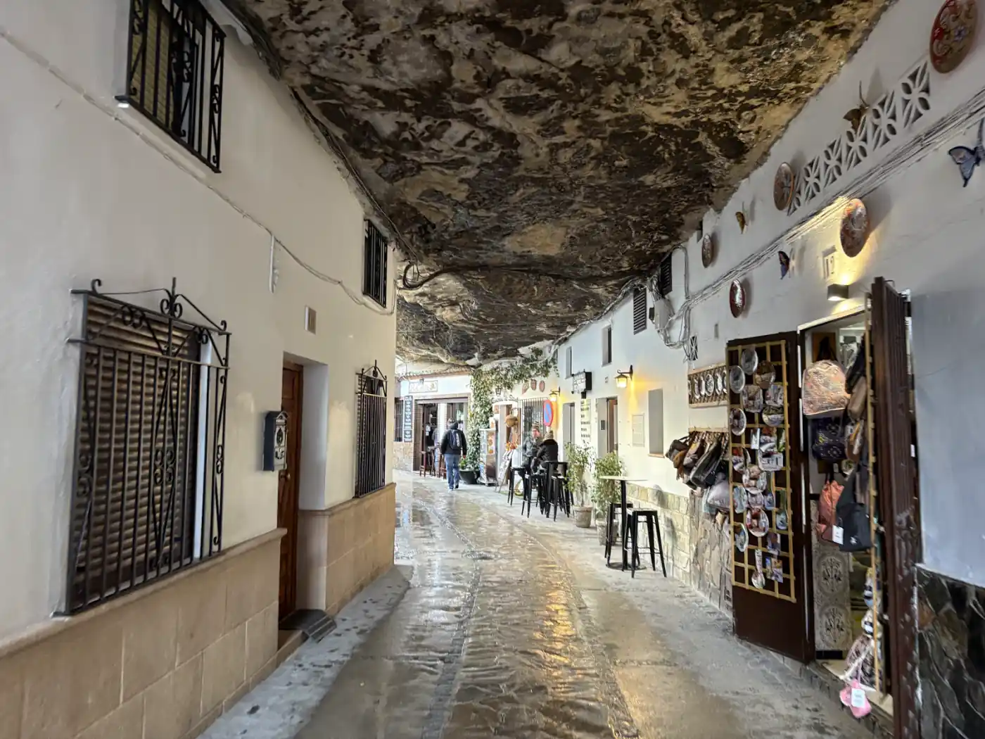 Schmale Gasse unter einem überhängenden Felsen in Setenil de las Bodegas mit weißen Häusern, Souvenirläden und Stehtischen