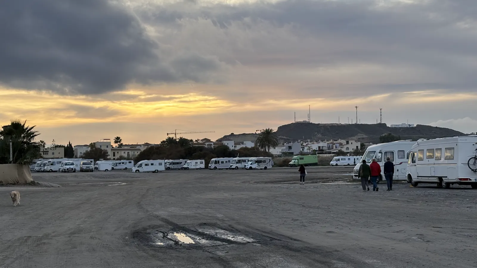 Weitläufiger unbefestigter Parkplatz in Südspanien bei bewölktem Abendhimmel, am Rand stehen zahlreiche Wohnmobile