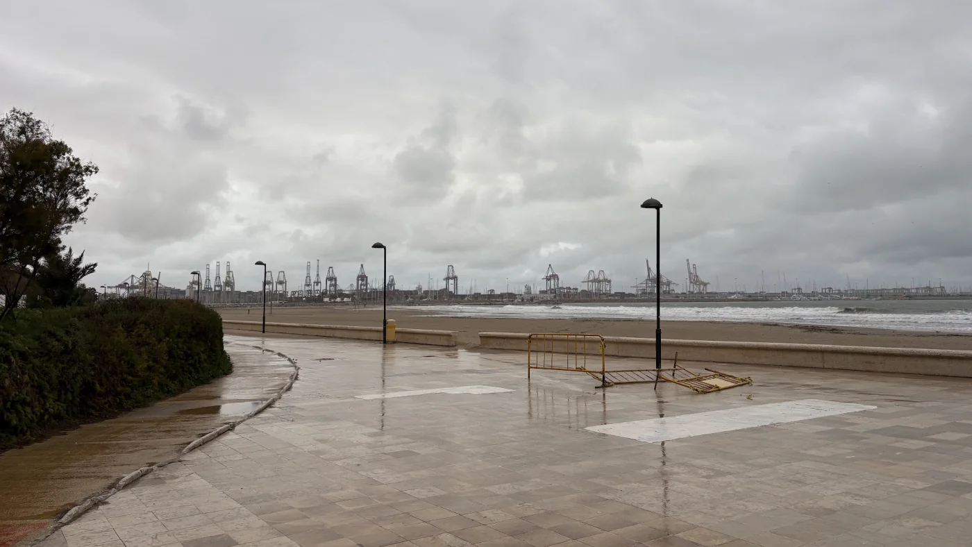 Nasse Strandpromenade südlich von Valencia bei grauem Himmel und aufgewühltem Meer, ein Absperrgitter liegt auf den Platten