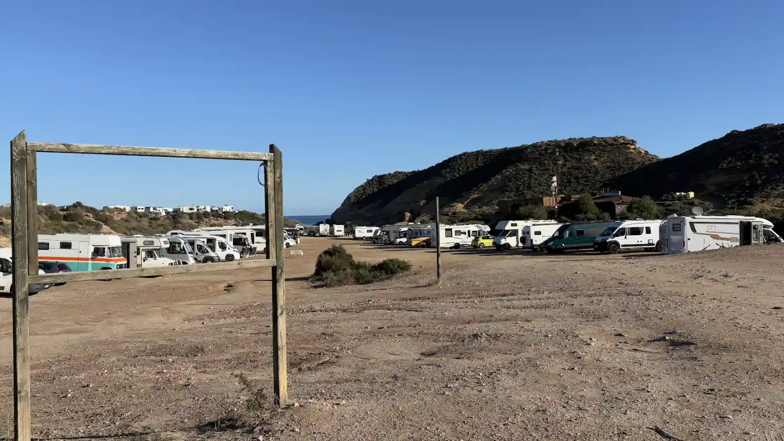 Große Schotterfläche in Südspanien mit Blick auf einen schmalen Meerstreifen, darauf stehen dicht an dicht Wohnmobile und Kastenwagen