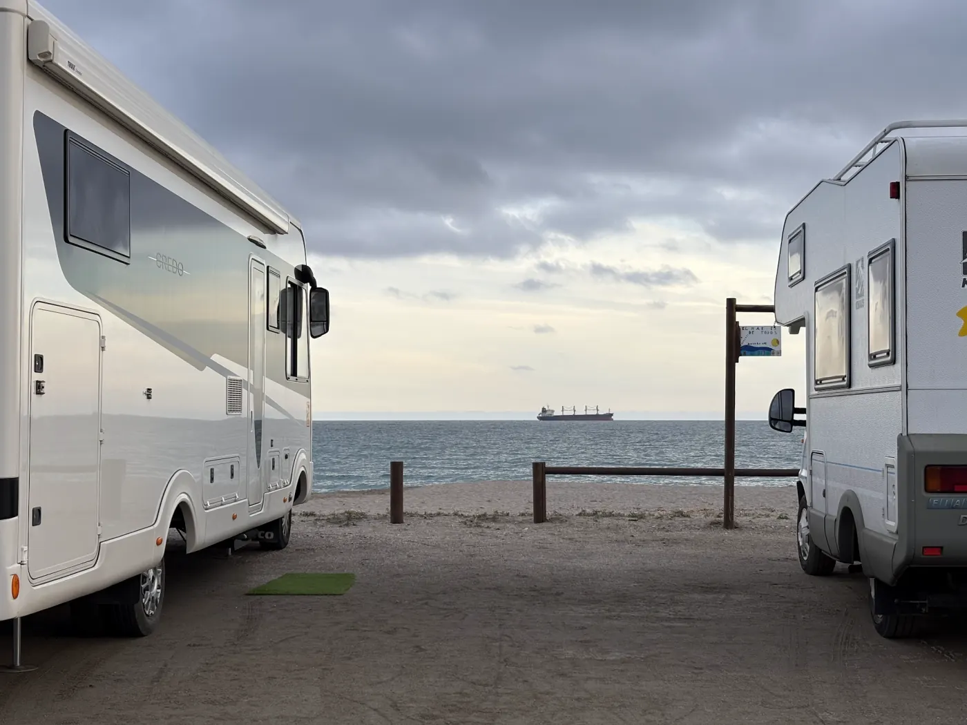 Zwei Wohnmobile auf einem öffentlichen Parkplatz direkt am Meer in Spanien mit Blick auf einen Frachter